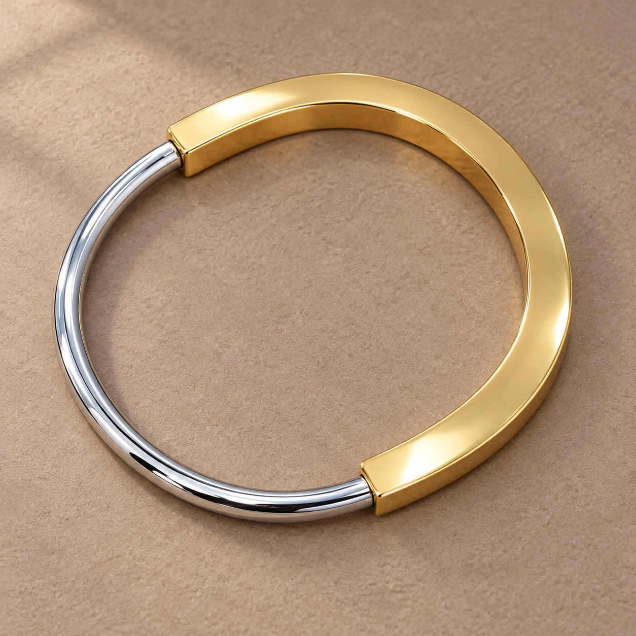 Two-tone 316L stainless steel kada bracelet with a gold-tone wide band and a silver-tone round wire section, lying flat on a beige surface, top view