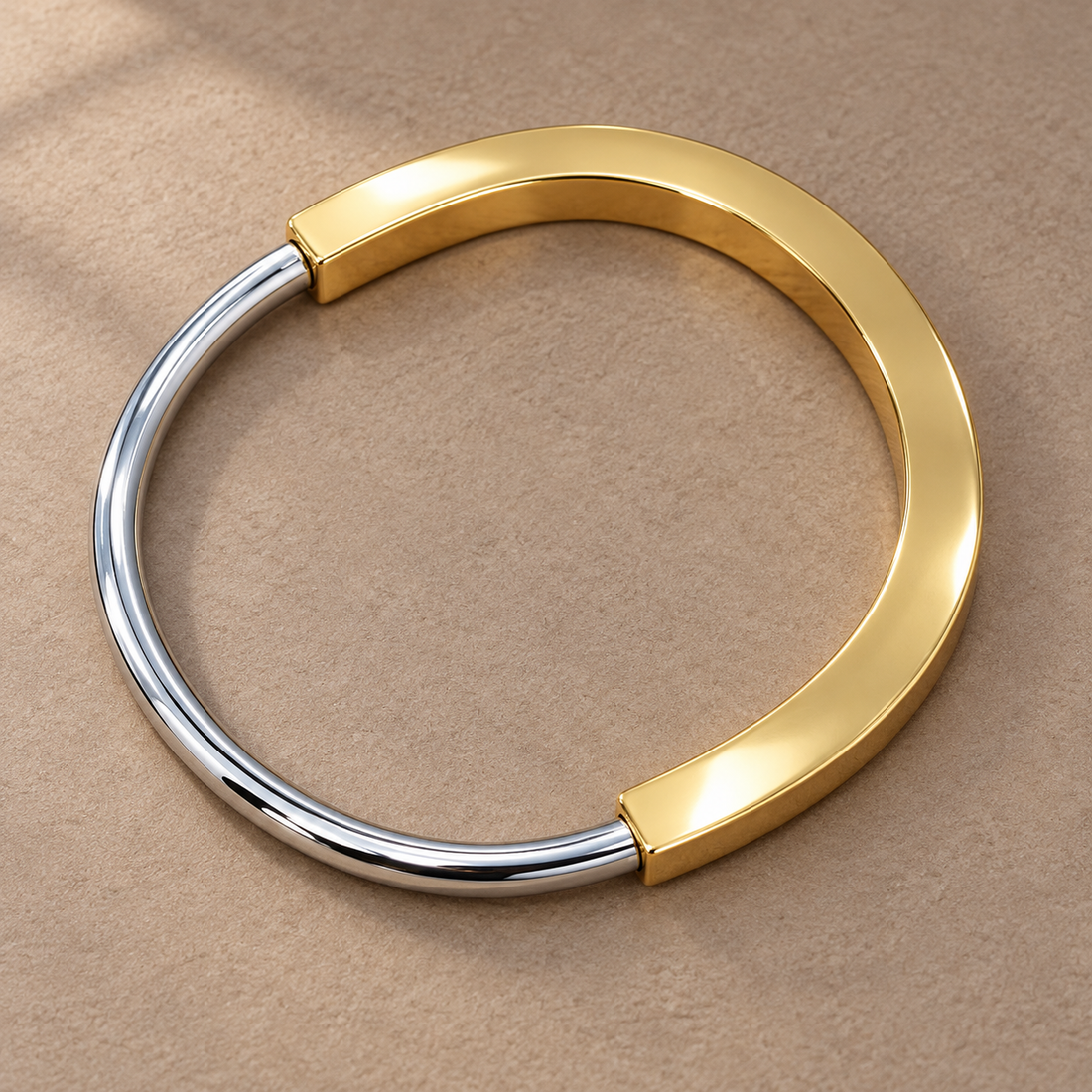 Two-tone 316L stainless steel kada bracelet with a gold-tone wide band and a silver-tone round wire section, lying flat on a beige surface, top view