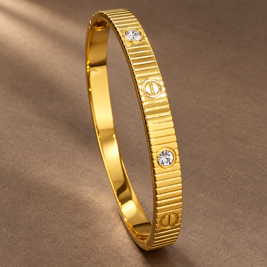 Gold-tone 304 stainless steel bangle bracelet with a ridged band, screw-head motifs and three crystal stones, shown lying at an angle