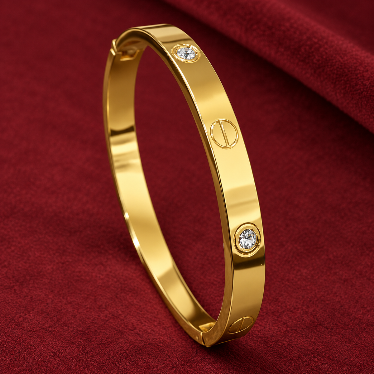 Gold-tone 304 stainless steel bangle bracelet with screw-head motifs and crystal-set studs on a hinged clasp, lying on a red fabric surface