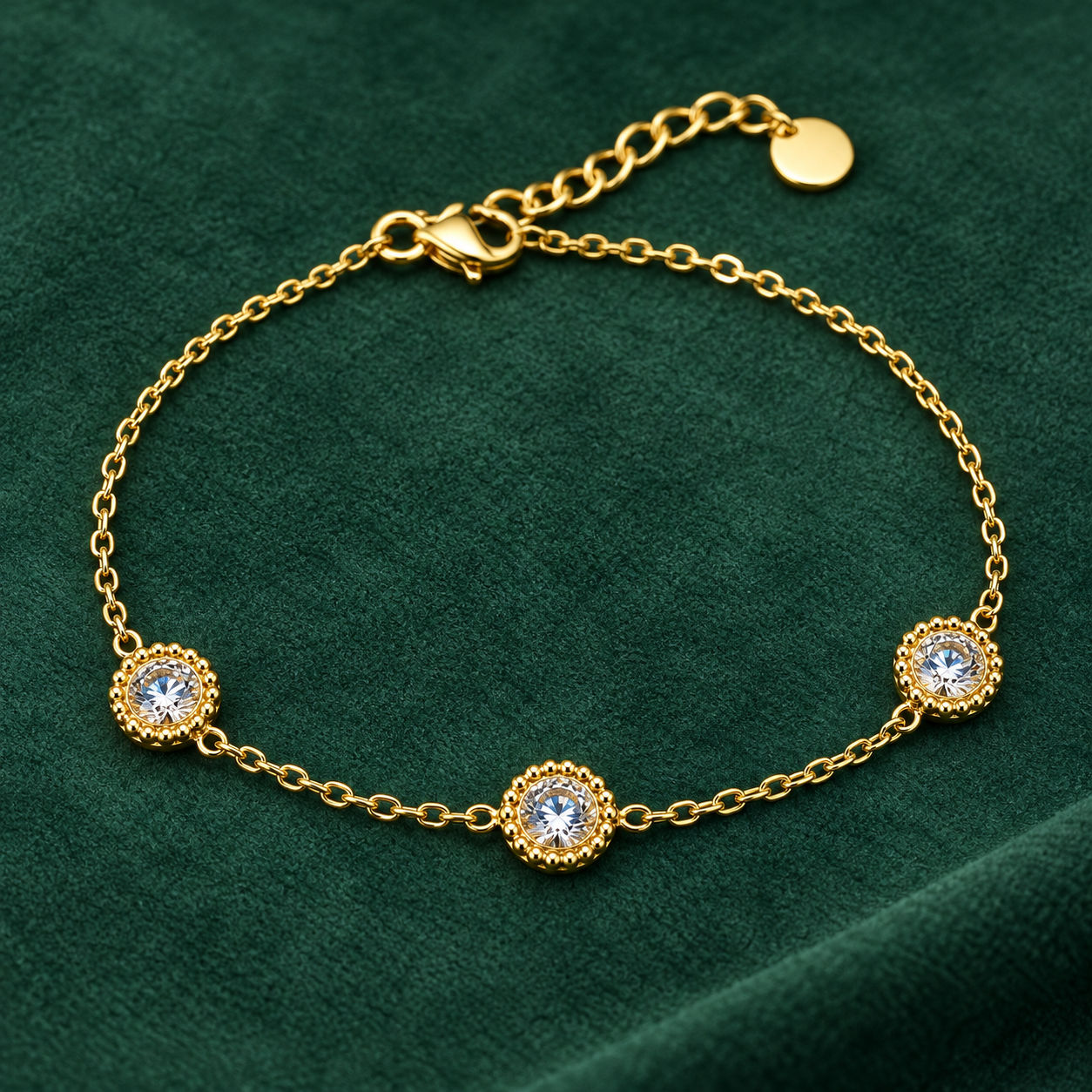 Gold-tone 316L chain bracelet with three round clear crystal stones in beaded settings, lobster clasp and extender tab, laid flat on green fabric