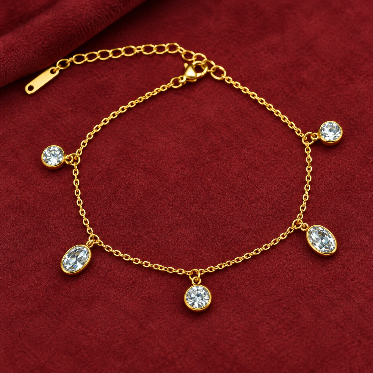 Gold-tone 304 stainless steel chain bracelet with five bezel-set clear crystal drops hanging from a fine cable chain, lying flat on red fabric