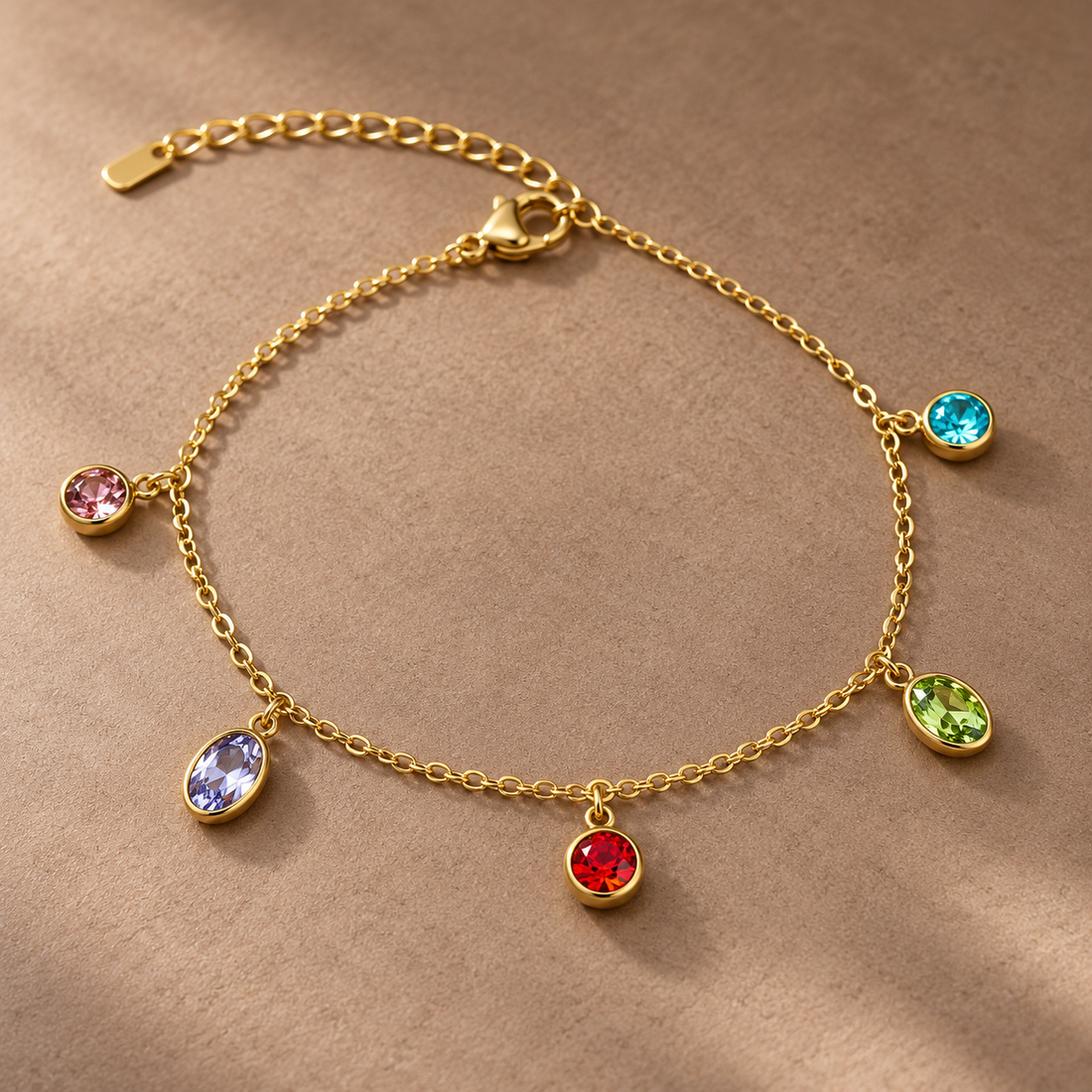 Gold-tone 304 stainless steel chain bracelet with five bezel-set coloured crystal charms in pink, lilac, red, green and turquoise, flat lay