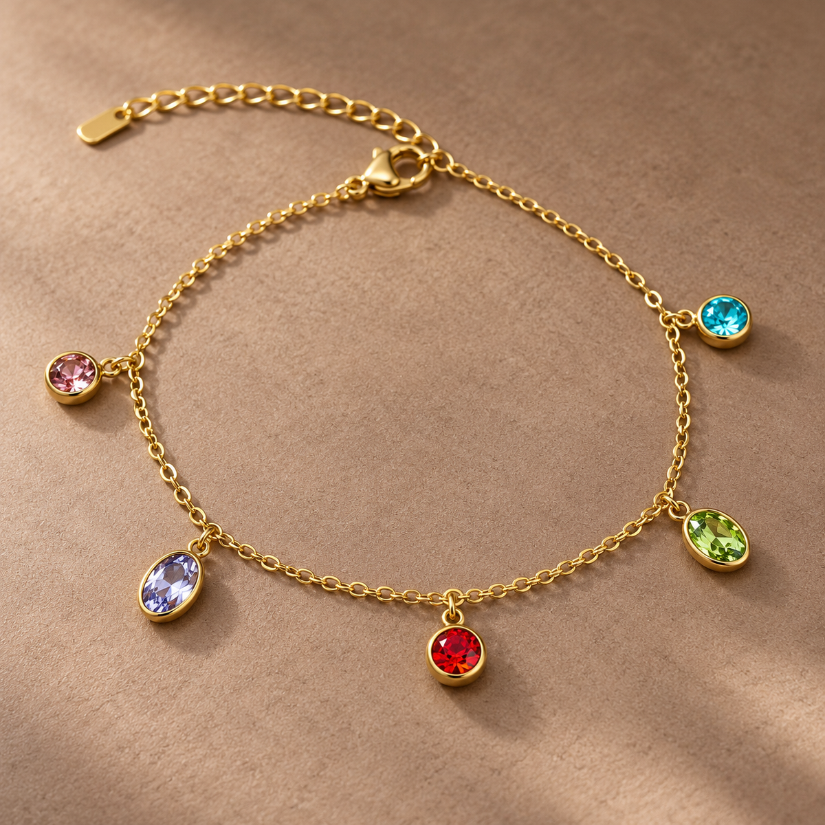 Gold-tone 304 stainless steel chain bracelet with five bezel-set coloured crystal charms in pink, lilac, red, green and turquoise, flat lay