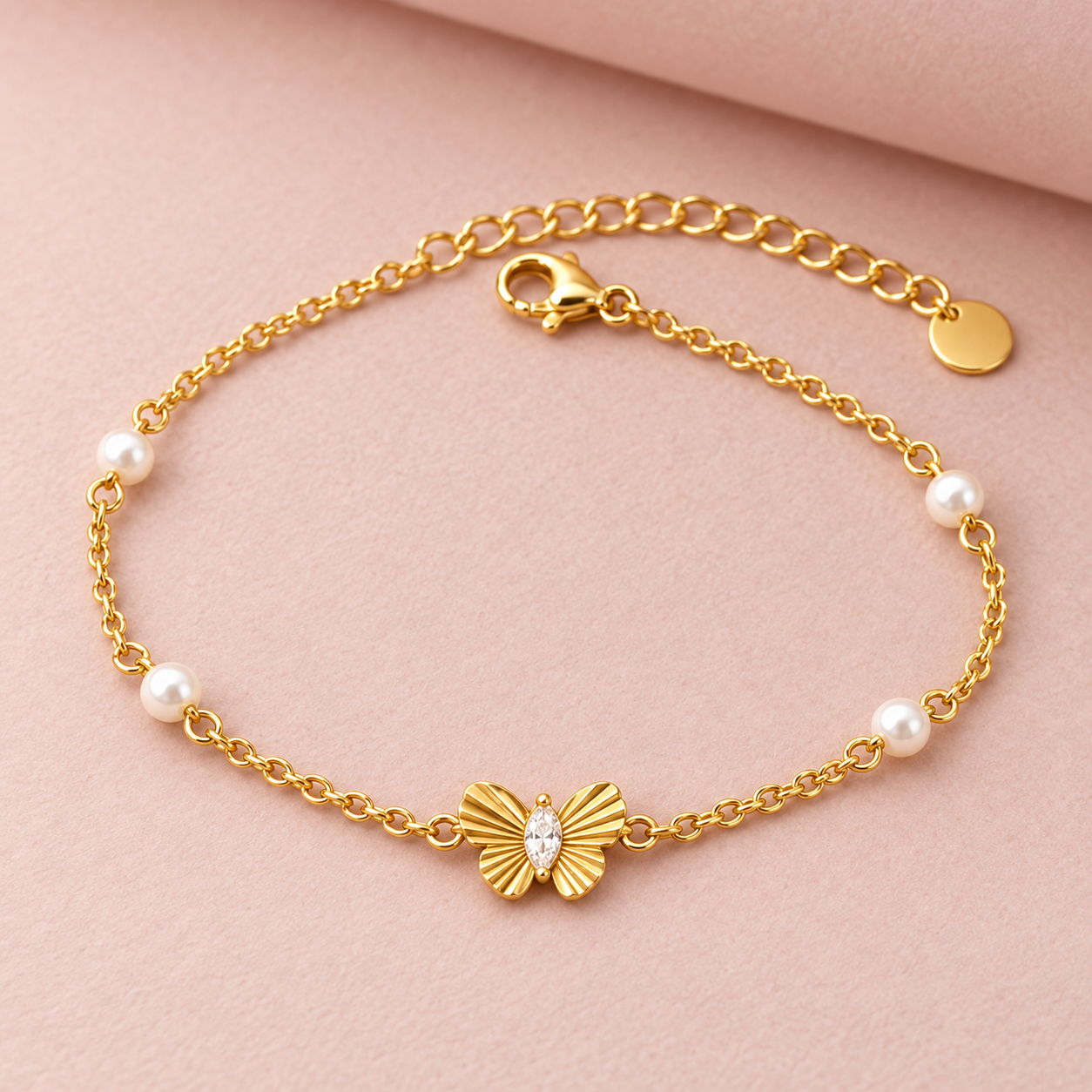 Gold-tone 316L stainless steel chain bracelet with a butterfly charm set with a clear marquise stone and small white pearls along the chain, flat lay