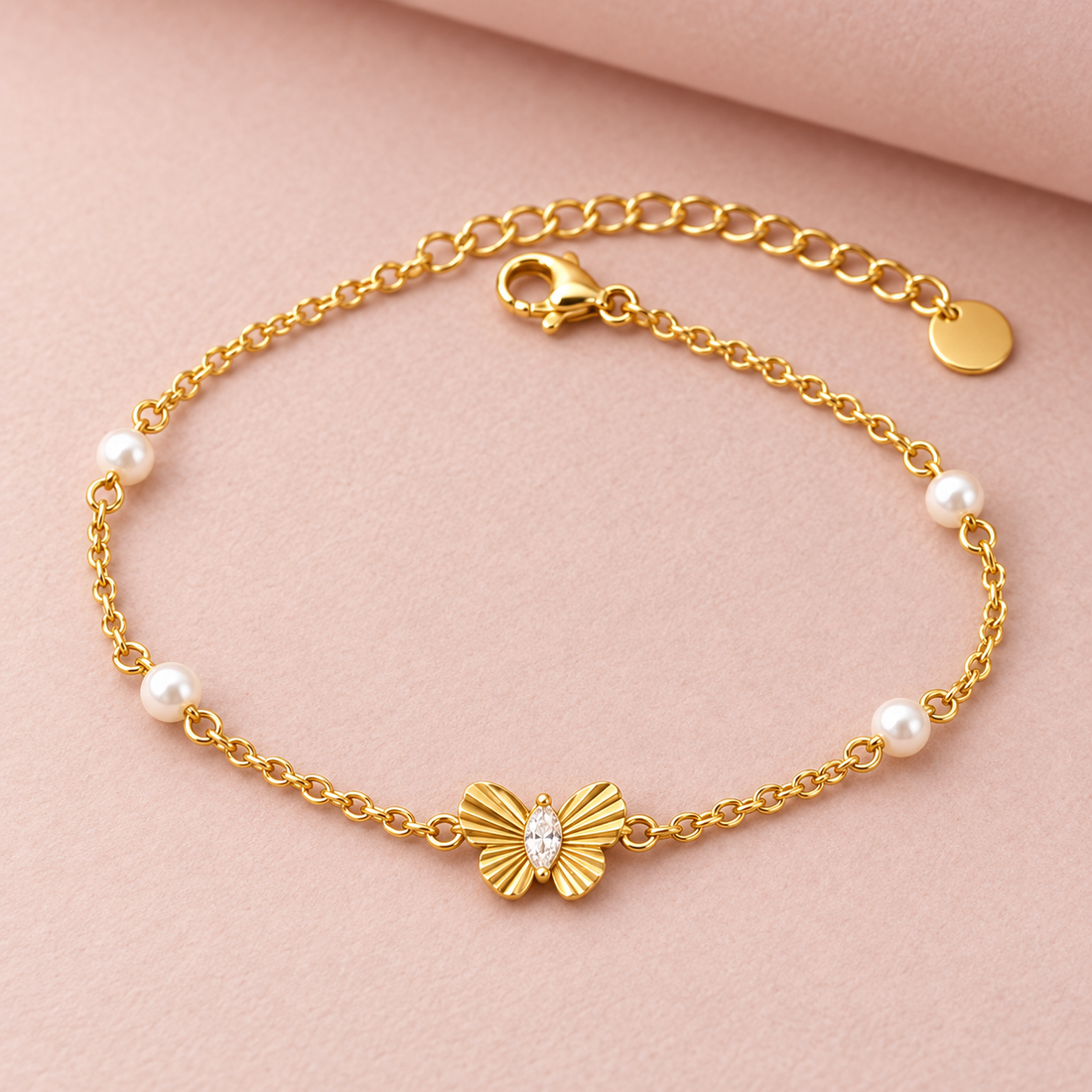Gold-tone 316L stainless steel chain bracelet with a butterfly charm set with a clear marquise stone and small white pearls along the chain, flat lay