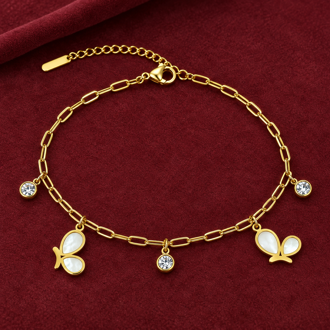 Gold-tone 304 stainless steel anklet with an oval link chain, two white shell butterfly charms and three crystal-set drops, laid flat on red velvet