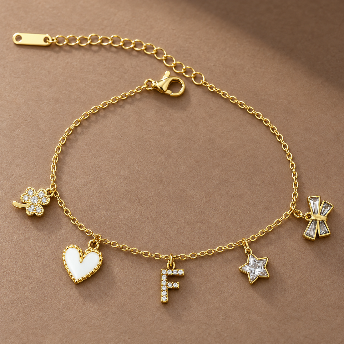 Gold-tone 304 stainless steel chain bracelet with a clover, white enamel heart, crystal-set F initial, crystal star and crystal bow charms, laid flat