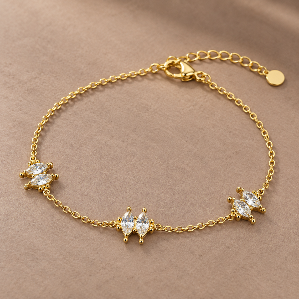 Gold-tone 316L stainless steel chain bracelet with three clusters of marquise-cut clear crystals and an extender tail, laid flat on a beige surface