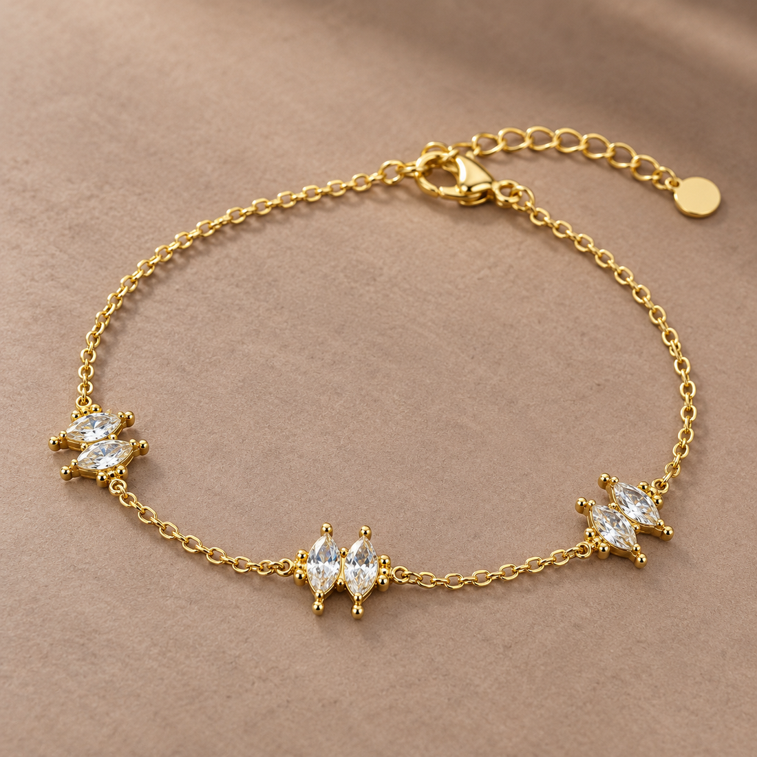 Gold-tone 316L stainless steel chain bracelet with three clusters of marquise-cut clear crystals and an extender tail, laid flat on a beige surface