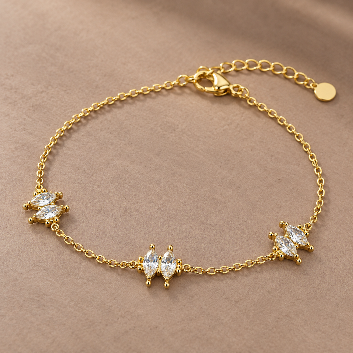 Gold-tone 316L stainless steel chain bracelet with three clusters of marquise-cut clear crystals and an extender tail, laid flat on a beige surface