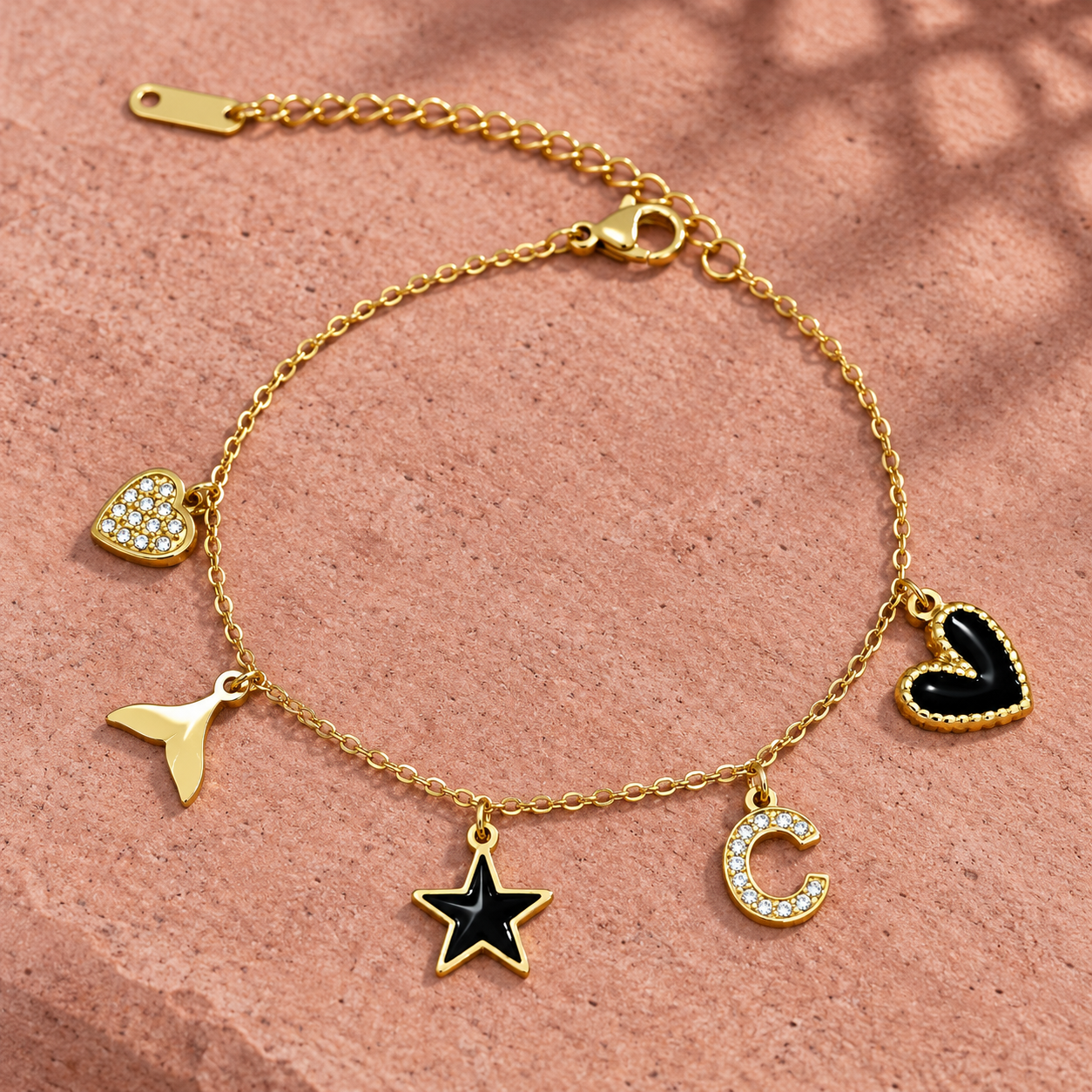 Gold-tone 304 stainless steel charm bracelet with a cable chain and five charms: crystal heart, tail, black enamel star, crystal C and black heart