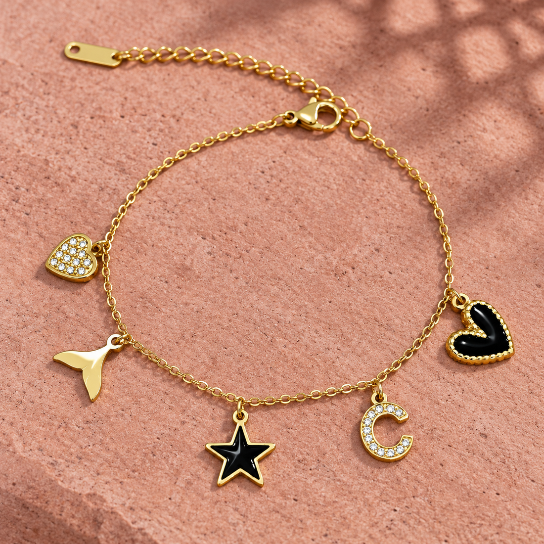 Gold-tone 304 stainless steel charm bracelet with a cable chain and five charms: crystal heart, tail, black enamel star, crystal C and black heart