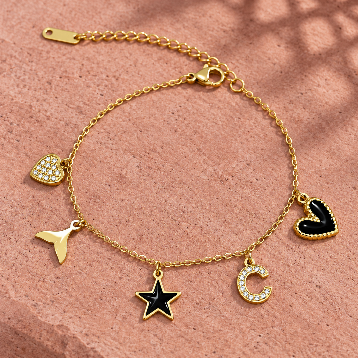 Gold-tone 304 stainless steel charm bracelet with a cable chain and five charms: crystal heart, tail, black enamel star, crystal C and black heart
