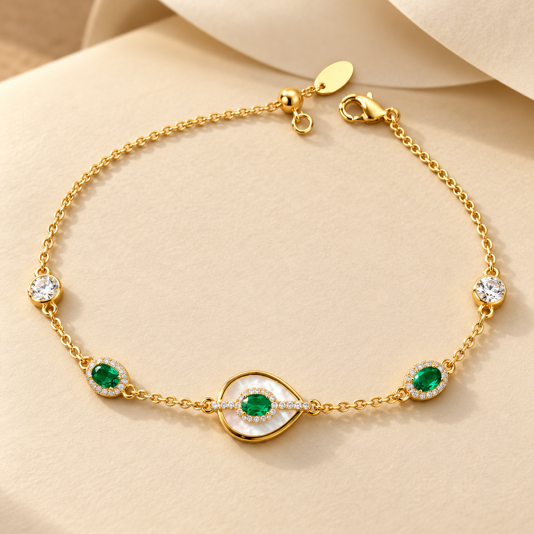 Gold-tone 316L stainless steel chain bracelet with a mother-of-pearl evil eye motif, green oval stones and white crystal accents, laid flat on a cream surface