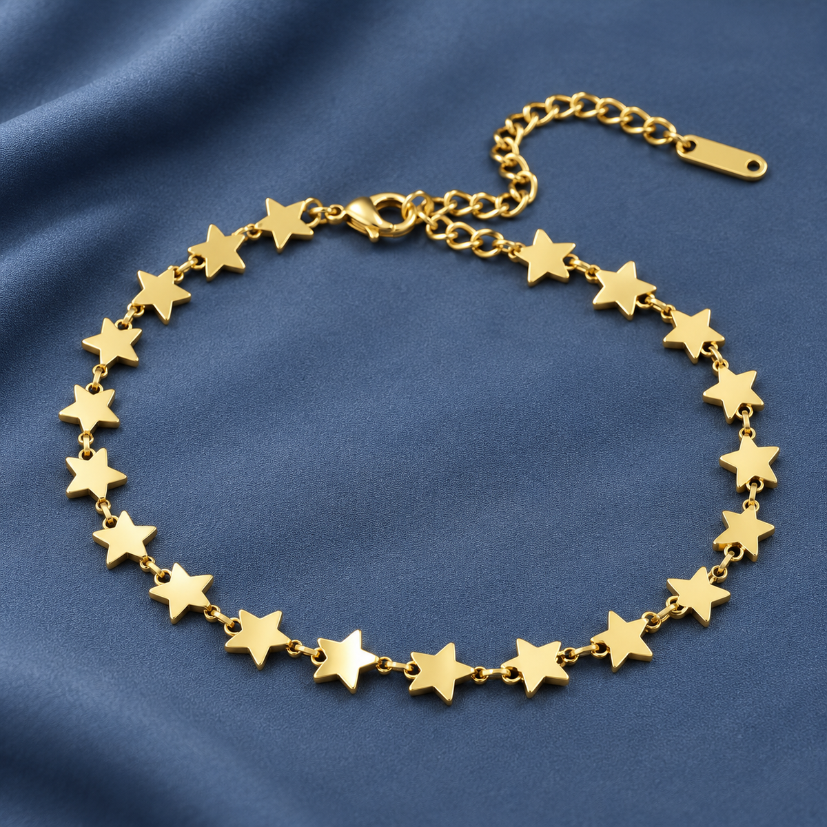 Gold-tone 304 stainless steel bracelet with flat star motifs linked by small chain, with a lobster clasp and extension chain, laid flat on blue fabric