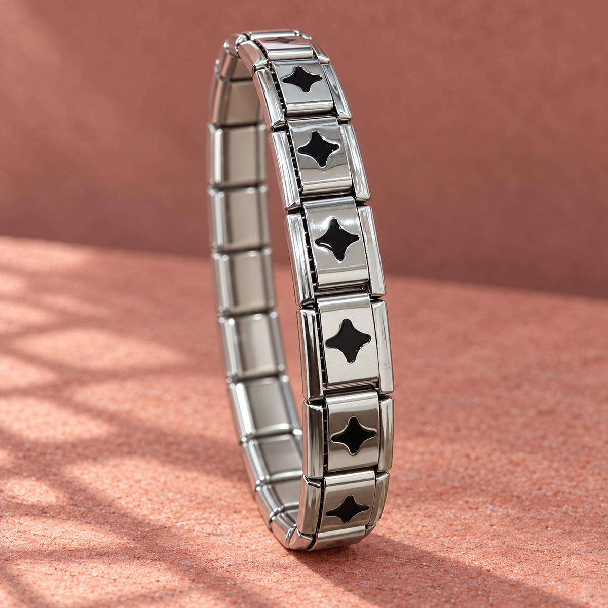 Silver-tone 304 stainless steel stretch bracelet with rectangular links and black four-point star enamel inserts, shown standing on a surface