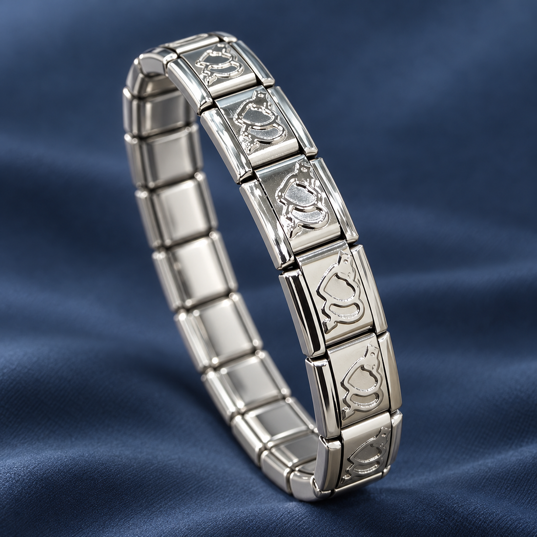 Silver-tone 304 stainless steel stretch bracelet with engraved cat-face motif links alternating with plain polished links, shown lying on blue fabric