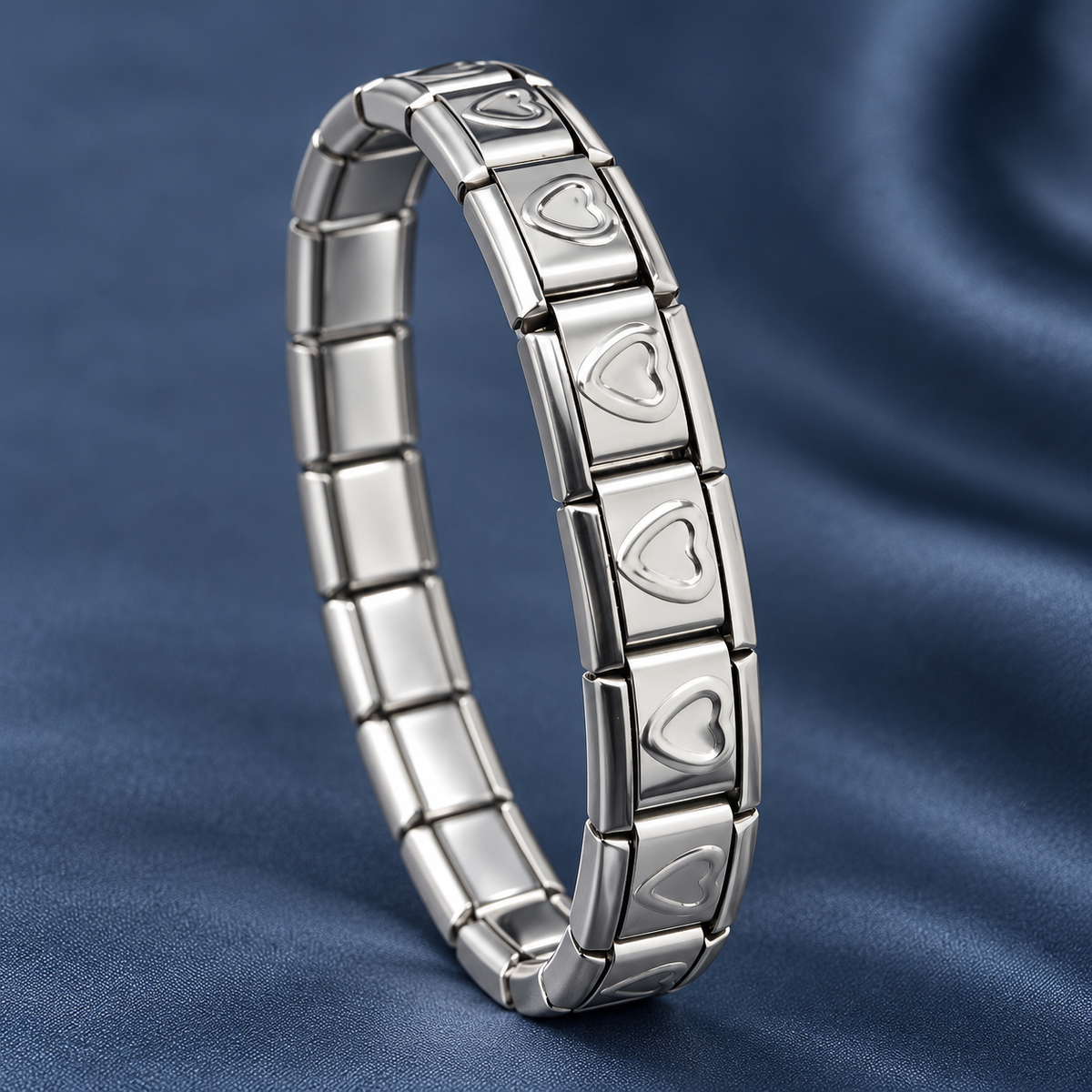 Silver-tone 304 stainless steel stretch bracelet with rectangular links, each engraved with an outlined heart, shown on a blue fabric background