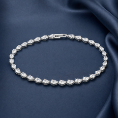 Silver-tone brass tennis bracelet with pear-cut clear crystal stones in claw settings, laid flat on navy fabric