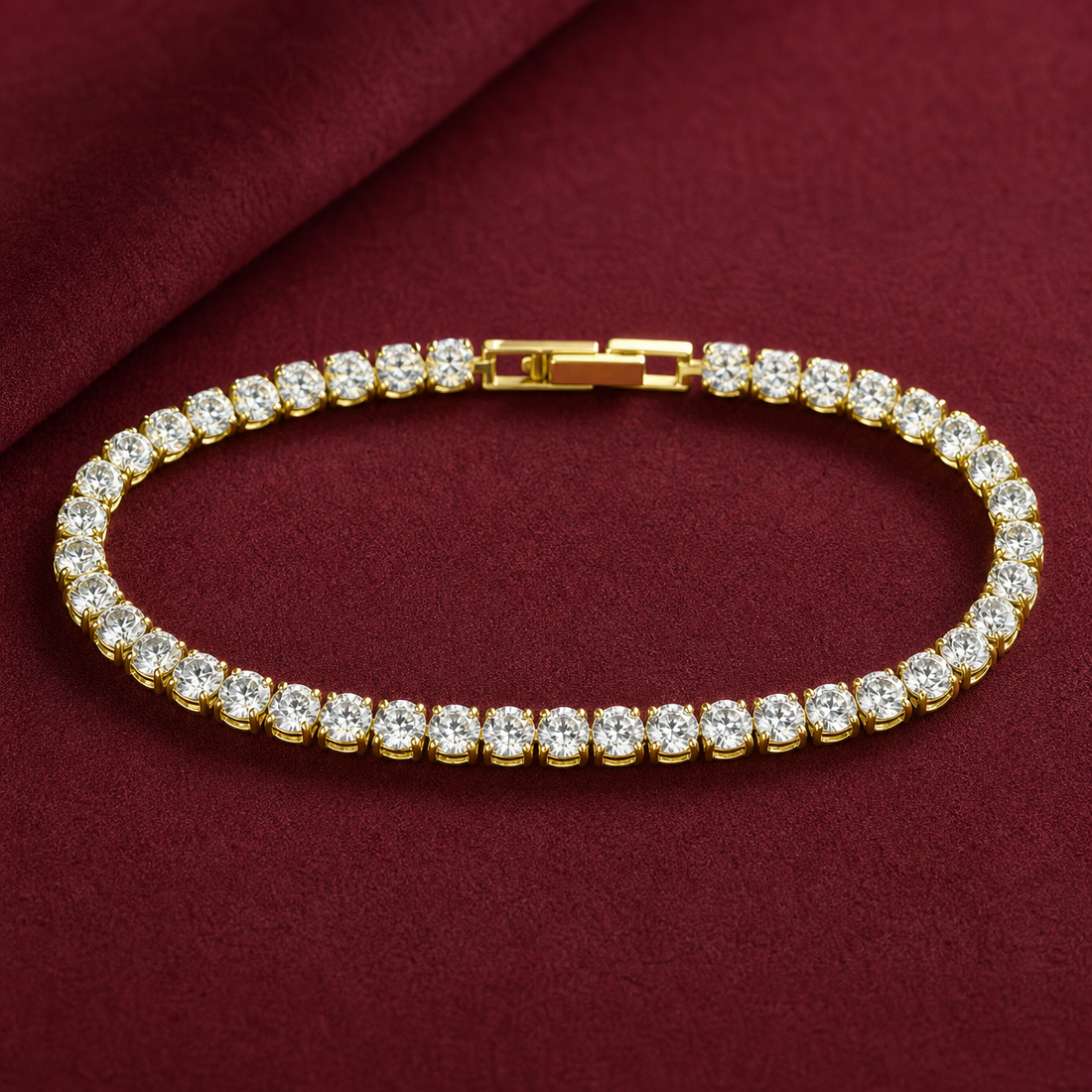 Gold-tone brass tennis bracelet with a row of round clear stones in claw settings and a box clasp, laid flat on a deep red cloth