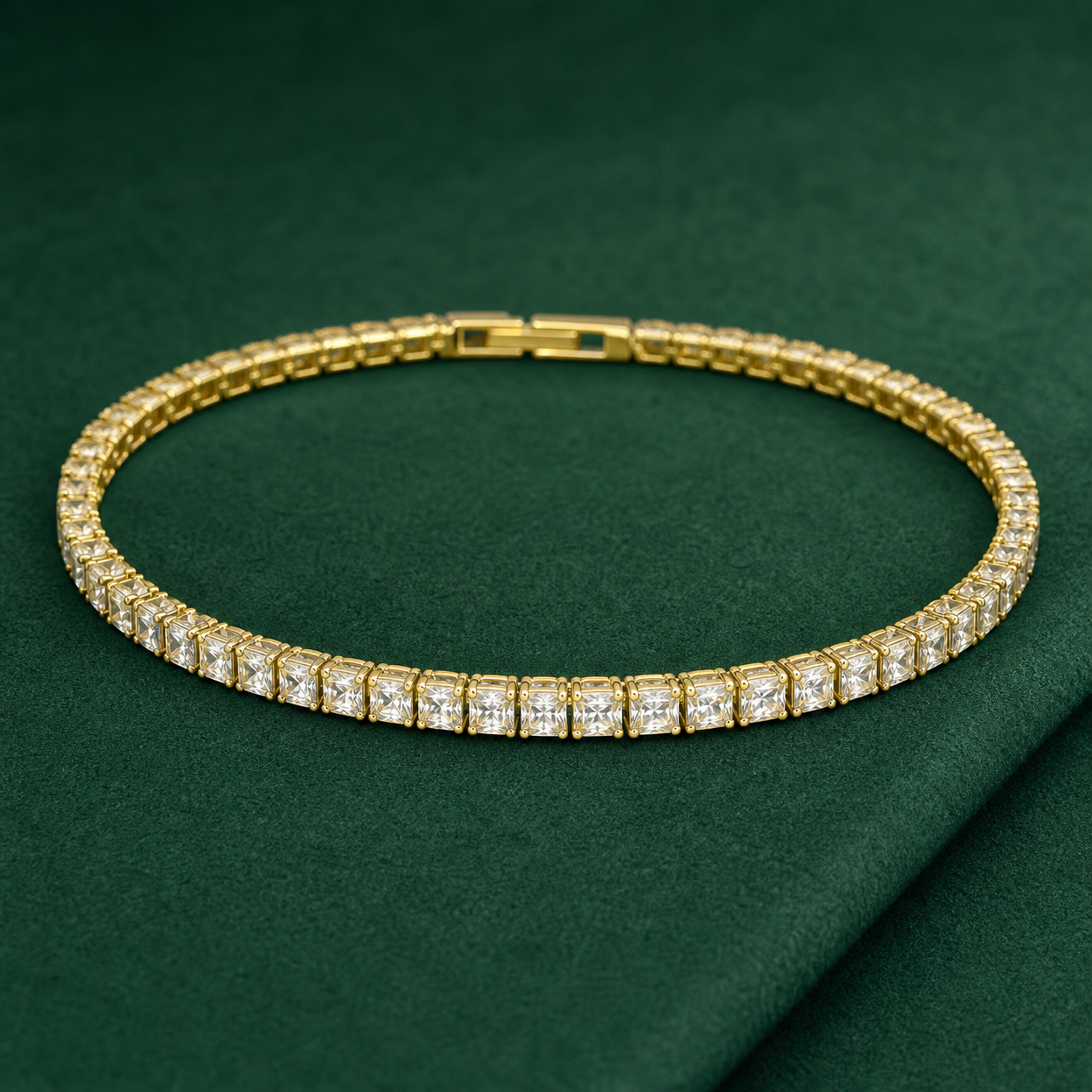 Gold-tone brass tennis bracelet with square clear stones in claw settings and a box clasp, laid flat on a green surface