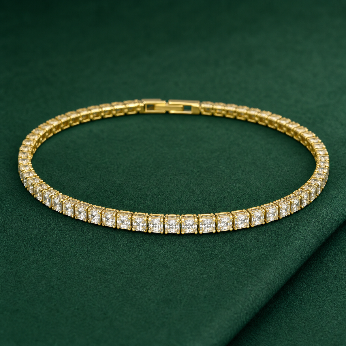 Gold-tone brass tennis bracelet with square clear stones in claw settings and a box clasp, laid flat on a green surface