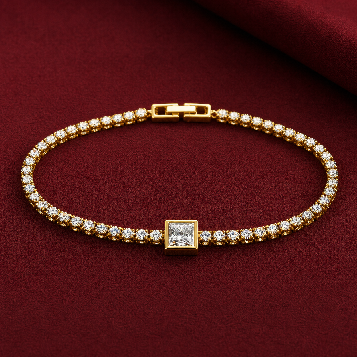 Gold-tone brass tennis bracelet with a row of round clear stones and a larger square-cut stone at the centre, laid flat on a dark red surface