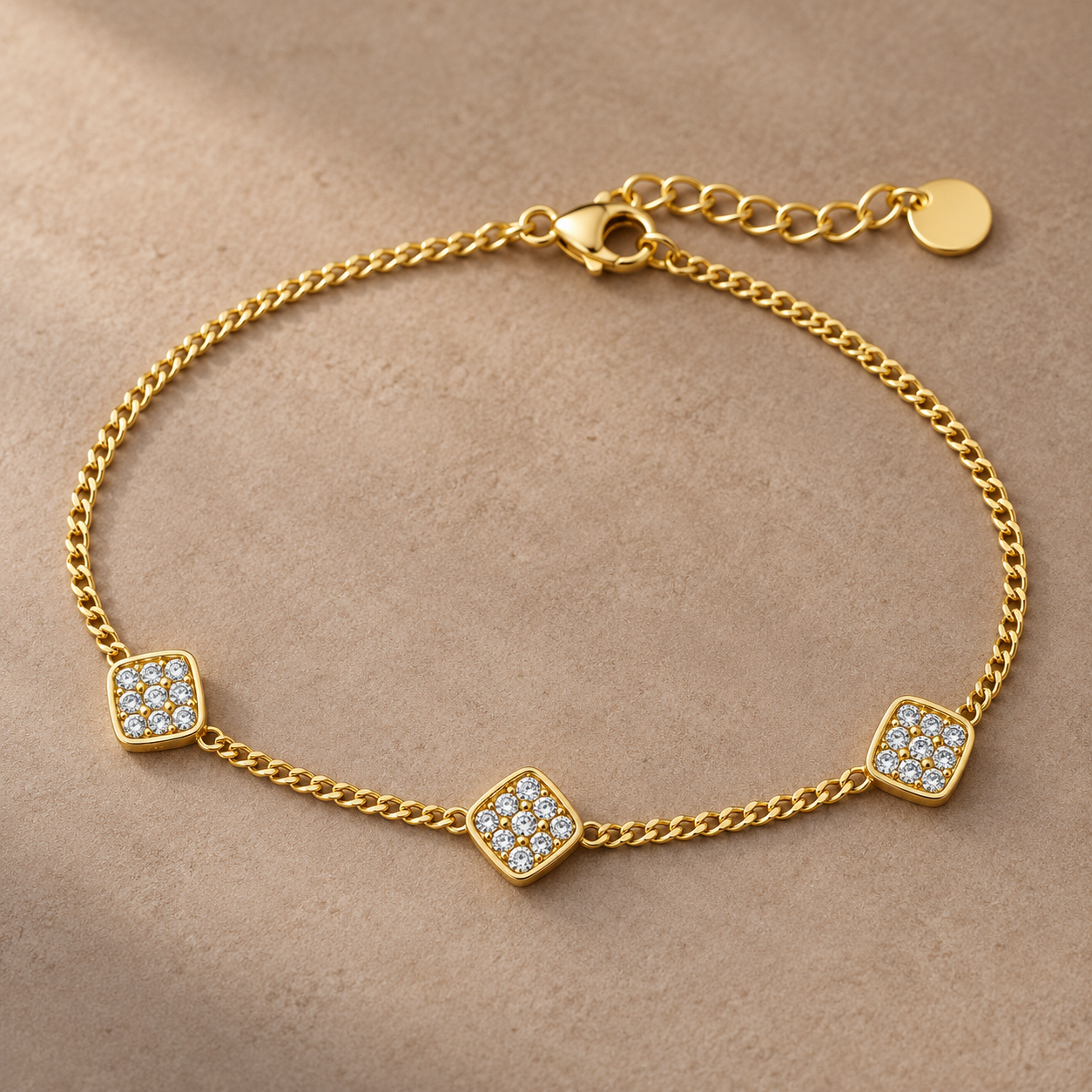 Gold-tone 316L curb chain bracelet with three square clusters of clear crystals and an adjustable extender with a round tag, laid flat