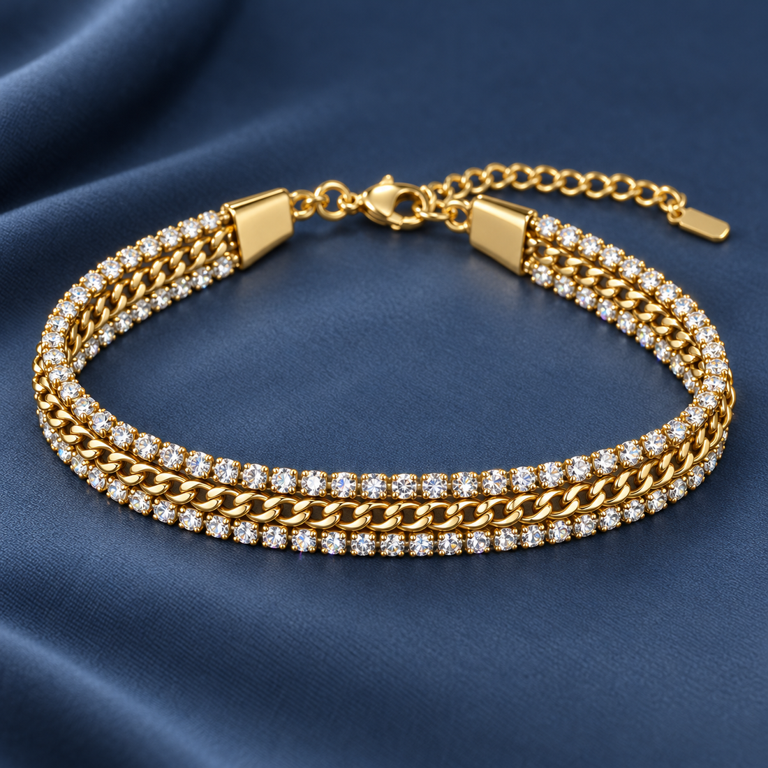 Gold-tone 316L stainless steel bracelet with a cuban link chain and two rows of crystal stones, laid flat on blue fabric