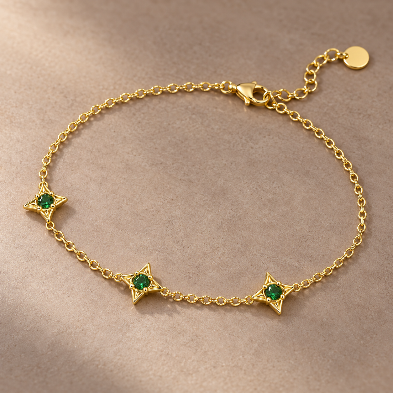 Gold-tone 316L stainless steel chain bracelet with three four-point star settings holding green stones, lobster clasp and extender tab, laid flat