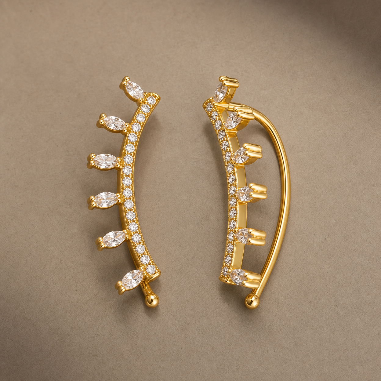 Gold-tone brass ear climber earrings with a curved row of marquise and round clear stones along the front, a pair shown from the front and side