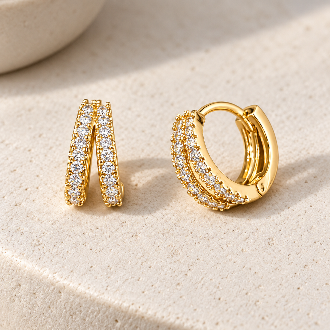 Gold-tone 316L stainless steel huggie earrings in a pair, each with a double row of clear stones set along the hoop, one shown open and one closed
