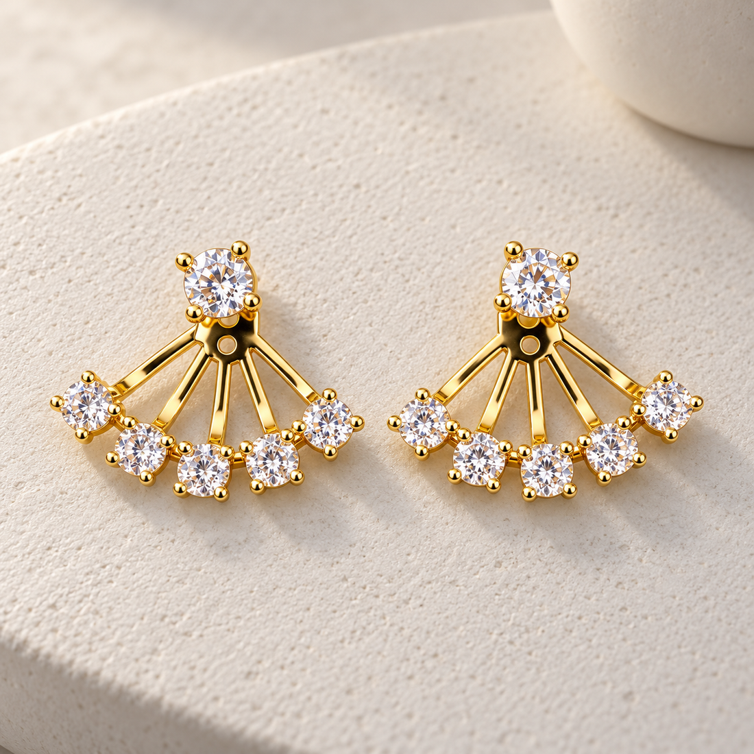 Gold-tone brass pair of fan-shaped ear jackets with clear crystal stones set along a curved fan, displayed on a textured stone surface