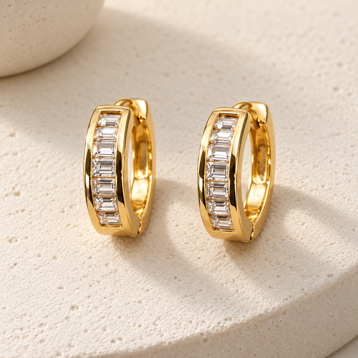 Gold-tone 316L stainless steel huggie hoop earrings, a pair, with a row of baguette-cut clear stones set along the front of each hoop