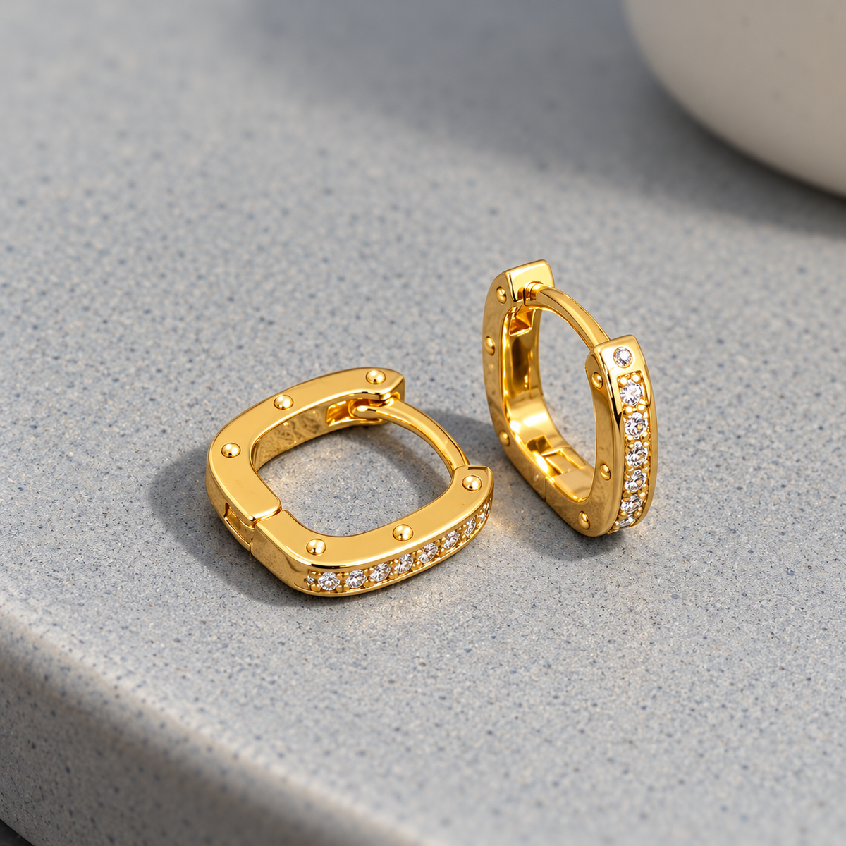 Gold-tone 304 stainless steel huggie earrings with a square-cornered hoop, a row of clear stones along one side and small dome studs, shown as a pair