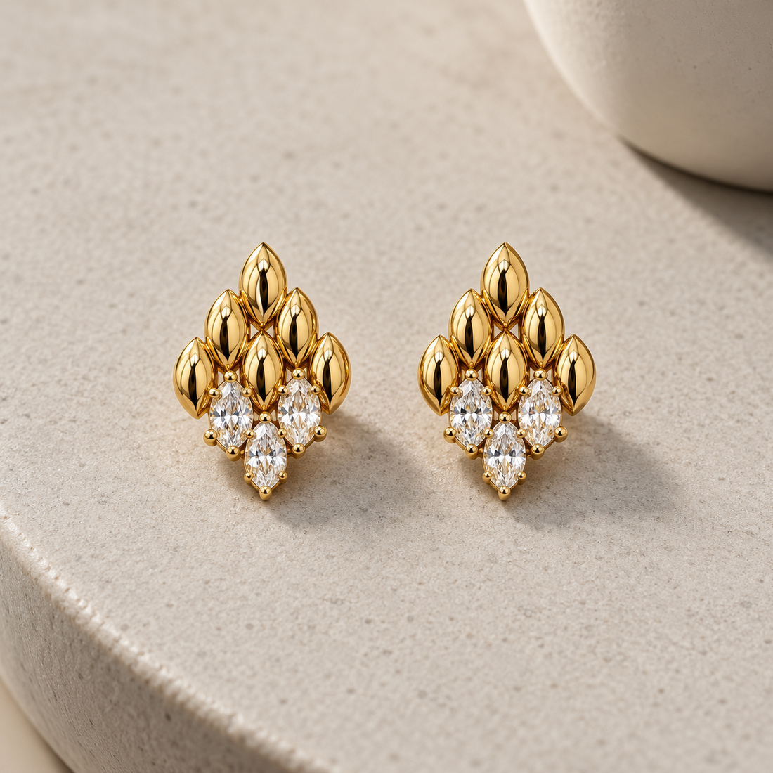 Gold-tone 316L stainless steel stud earrings with marquise-shaped petal motifs and clear marquise stones in a cluster, a pair shown on a stone surface