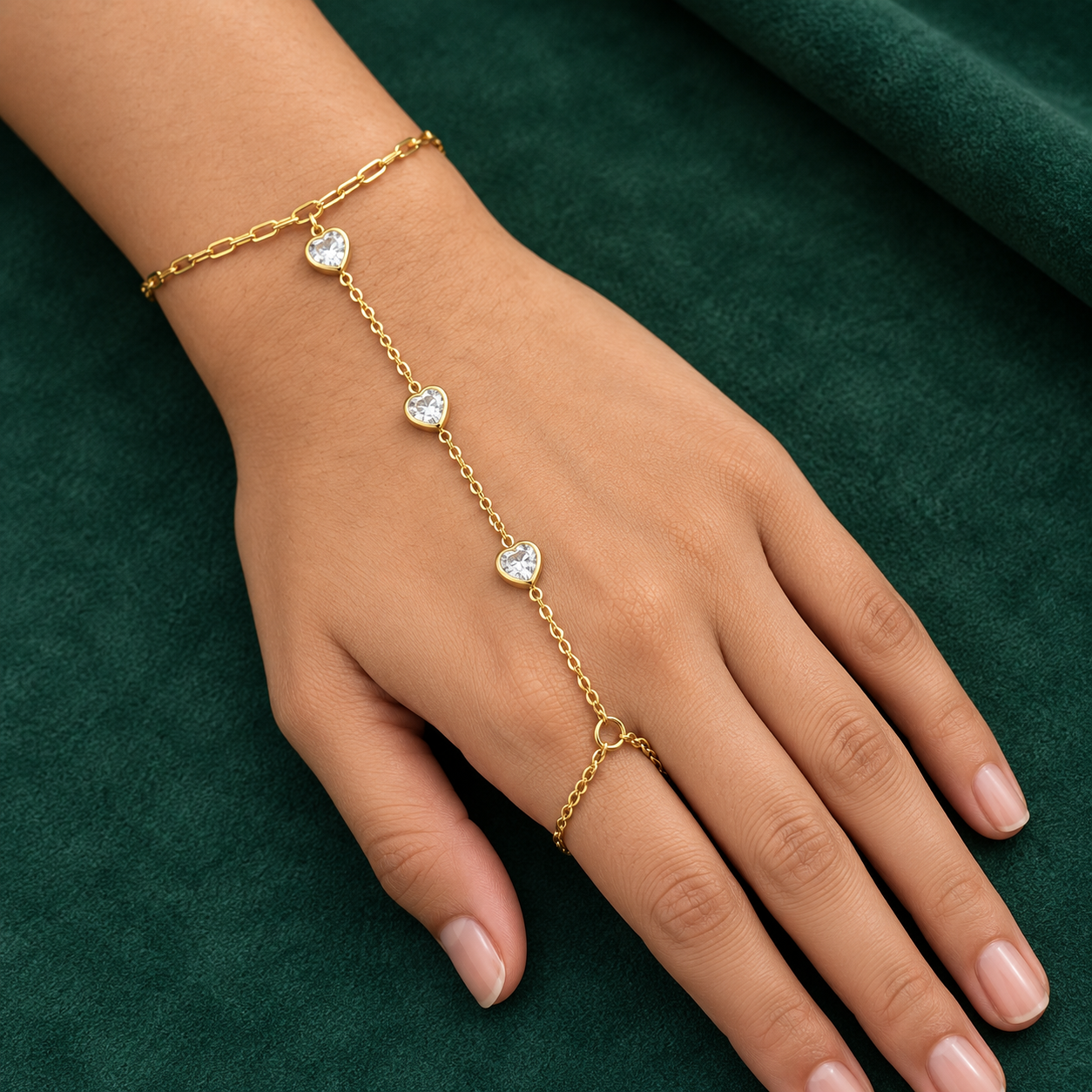 Gold-tone 304 stainless steel hand chain with three heart-shaped crystal stones on a fine chain, a ring link on the finger, worn on a hand