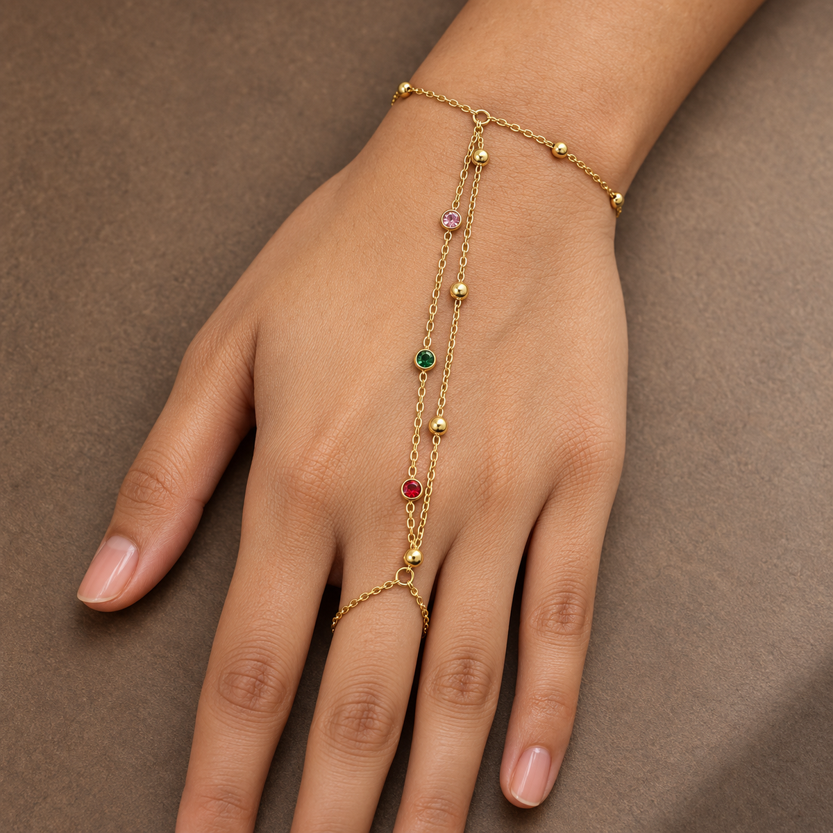 Gold-tone 304 stainless steel hand chain with a bracelet, a ring link and a double chain drop set with pink, green and red crystals, worn on a hand