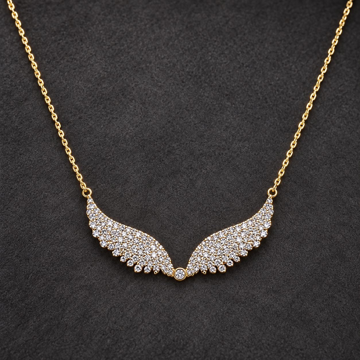 Gold-tone 316L stainless steel necklace with a fine cable chain and a pendant of two wings set with clear stones, laid flat on a dark surface