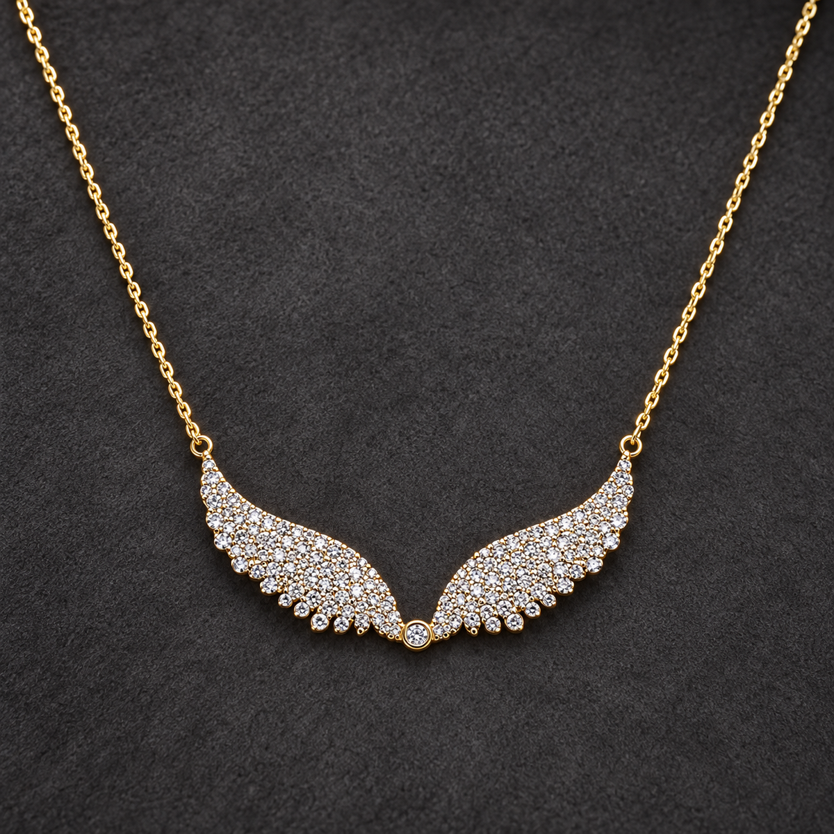 Gold-tone 316L stainless steel necklace with a fine cable chain and a pendant of two wings set with clear stones, laid flat on a dark surface