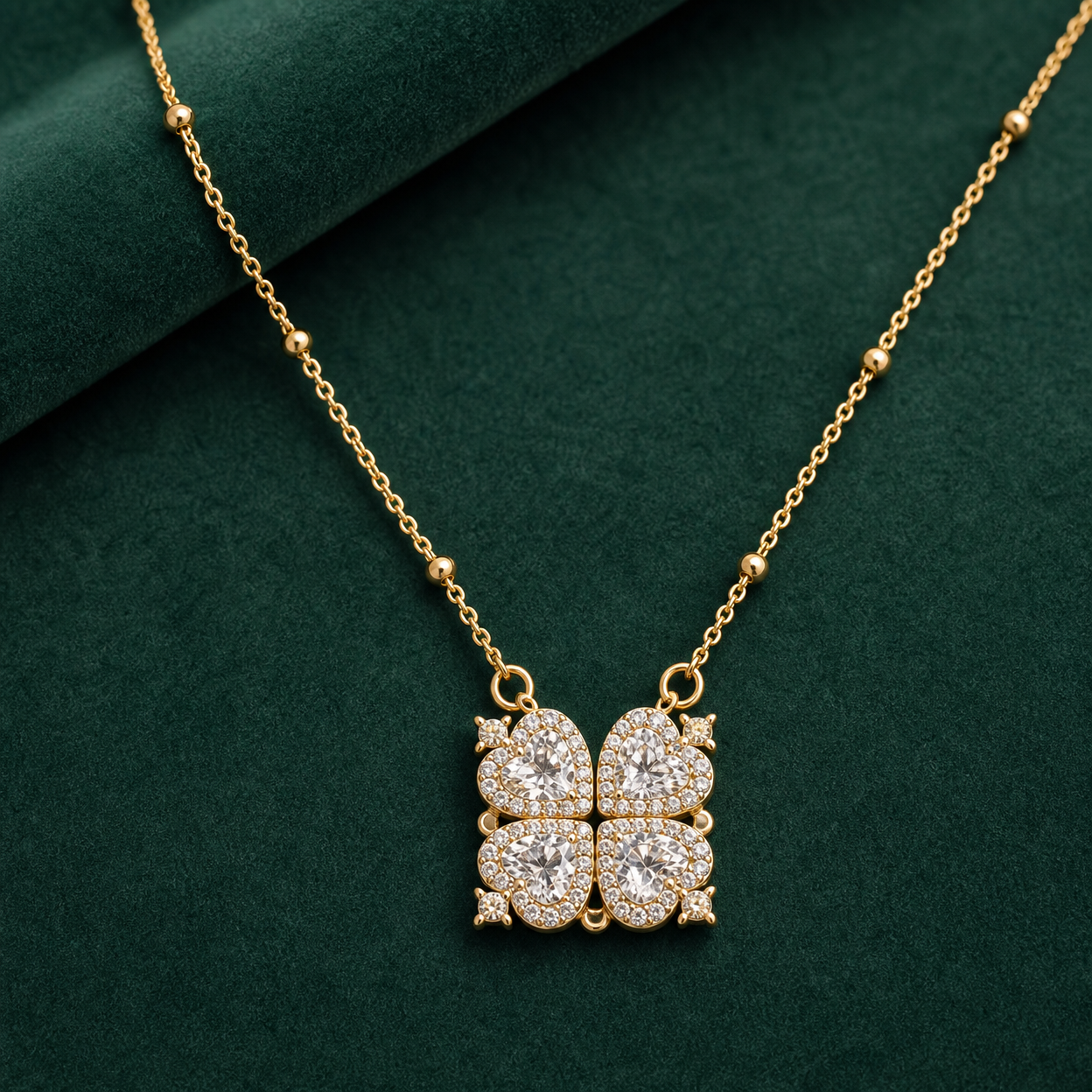 Gold-tone 304 stainless steel necklace with a four-heart clover pendant set with white stones on a bead-accent chain, on a green surface