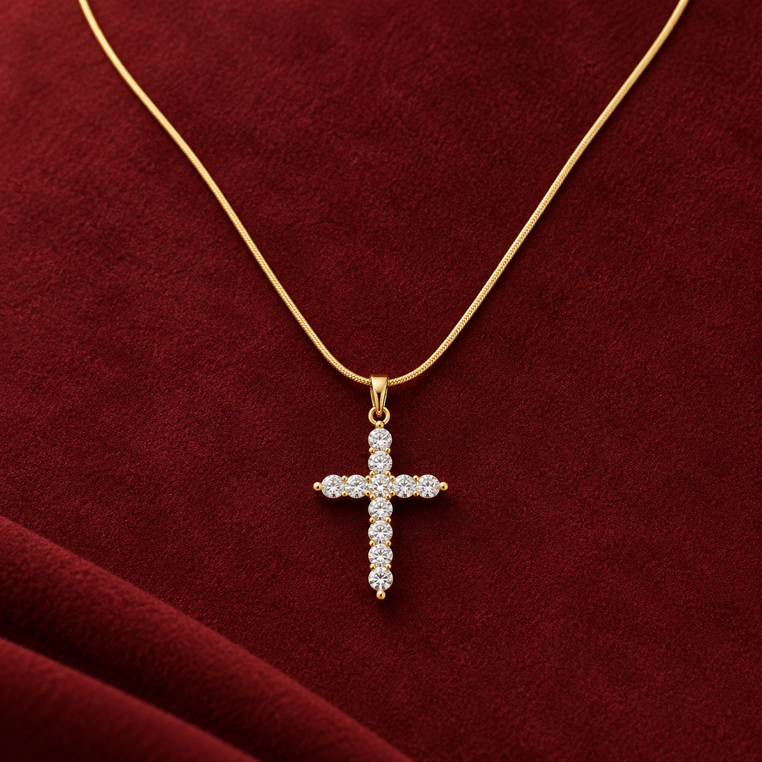 Gold-tone 316L stainless steel pendant necklace with a cross set with clear stones on a fine snake chain, shown on a red velvet surface