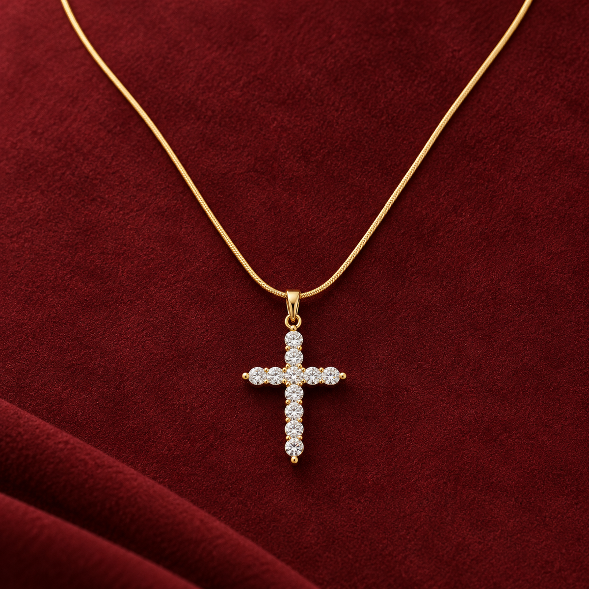 Gold-tone 316L stainless steel pendant necklace with a cross set with clear stones on a fine snake chain, shown on a red velvet surface