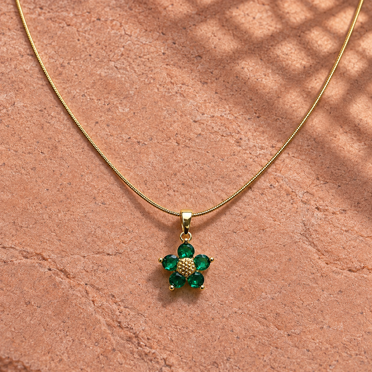 Gold-tone 316L stainless steel pendant necklace with a five-stone green flower pendant on a snake chain, laid on a stone surface