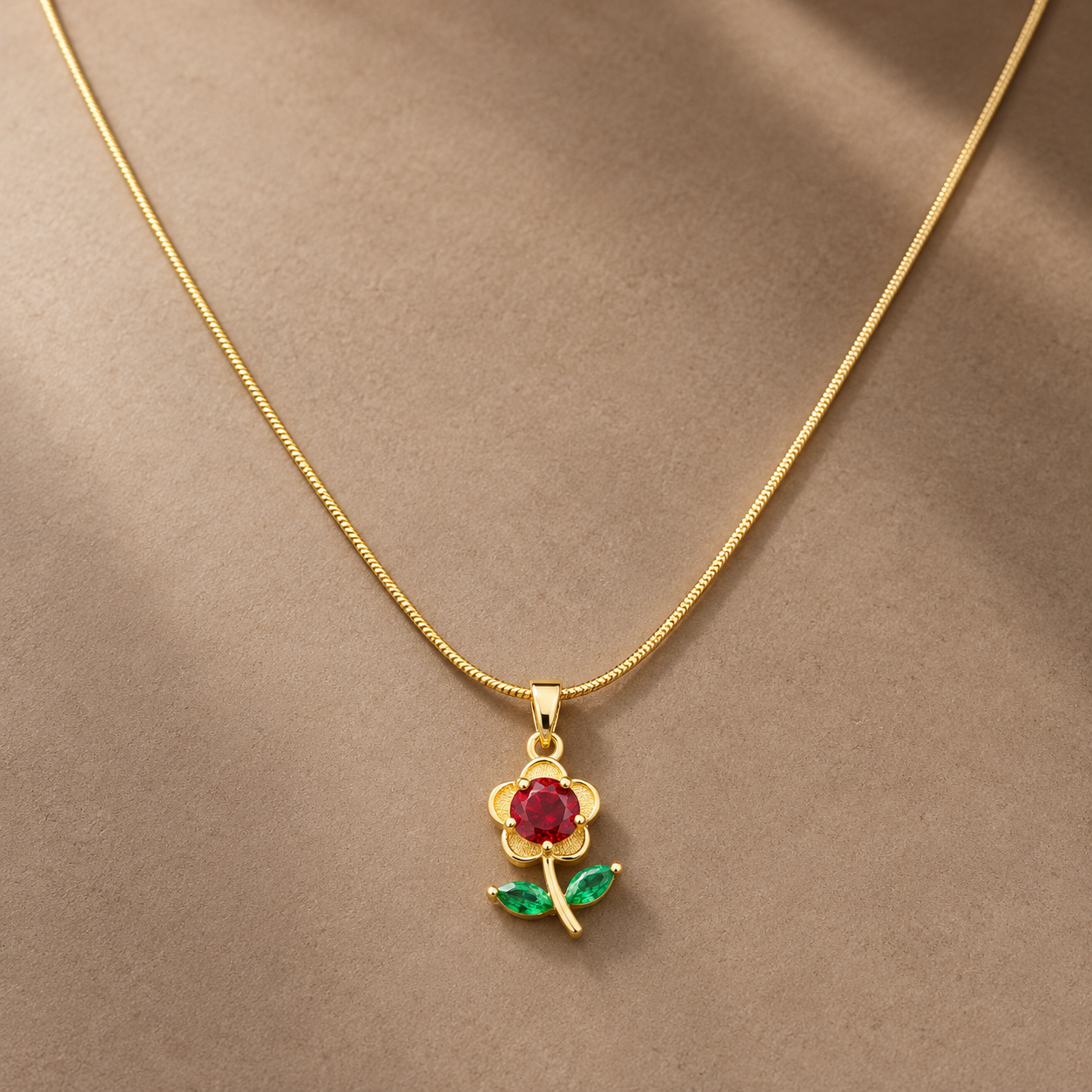 Gold-tone 316L stainless steel flower pendant necklace with a red round stone centre and green marquise leaves on a thin snake chain, worn at the neck
