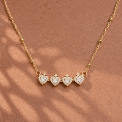 Gold-tone 304 stainless steel necklace with four heart pendants set with clear stones and a small crown stone on top, on a beaded chain, flat view
