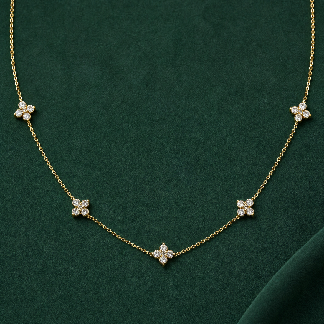 Gold-tone 316L stainless steel necklace with five clustered crystal flower motifs spaced along a fine cable chain, laid flat on a green surface