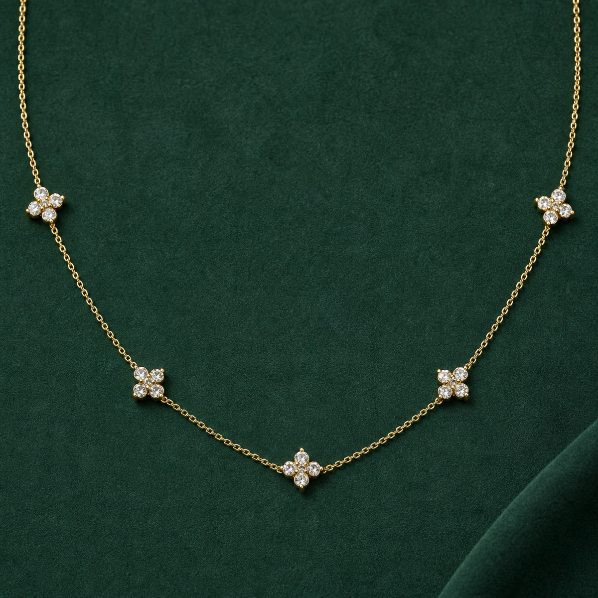 Gold-tone 316L stainless steel necklace with five clustered crystal flower motifs spaced along a fine cable chain, laid flat on a green surface