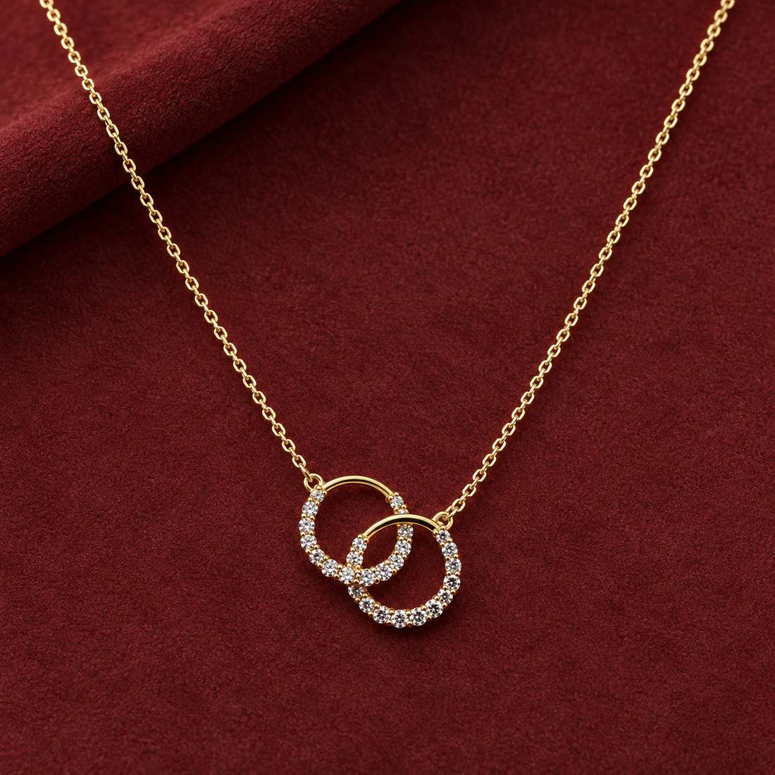 Gold-tone 316L stainless steel necklace with two interlocked open rings set with clear crystals on a fine cable chain, laid flat on a red cloth